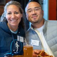Two event attendees sitting at table with food, leaning towards each other and smiling for photo